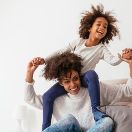 mother and daughter happily play on a large bed